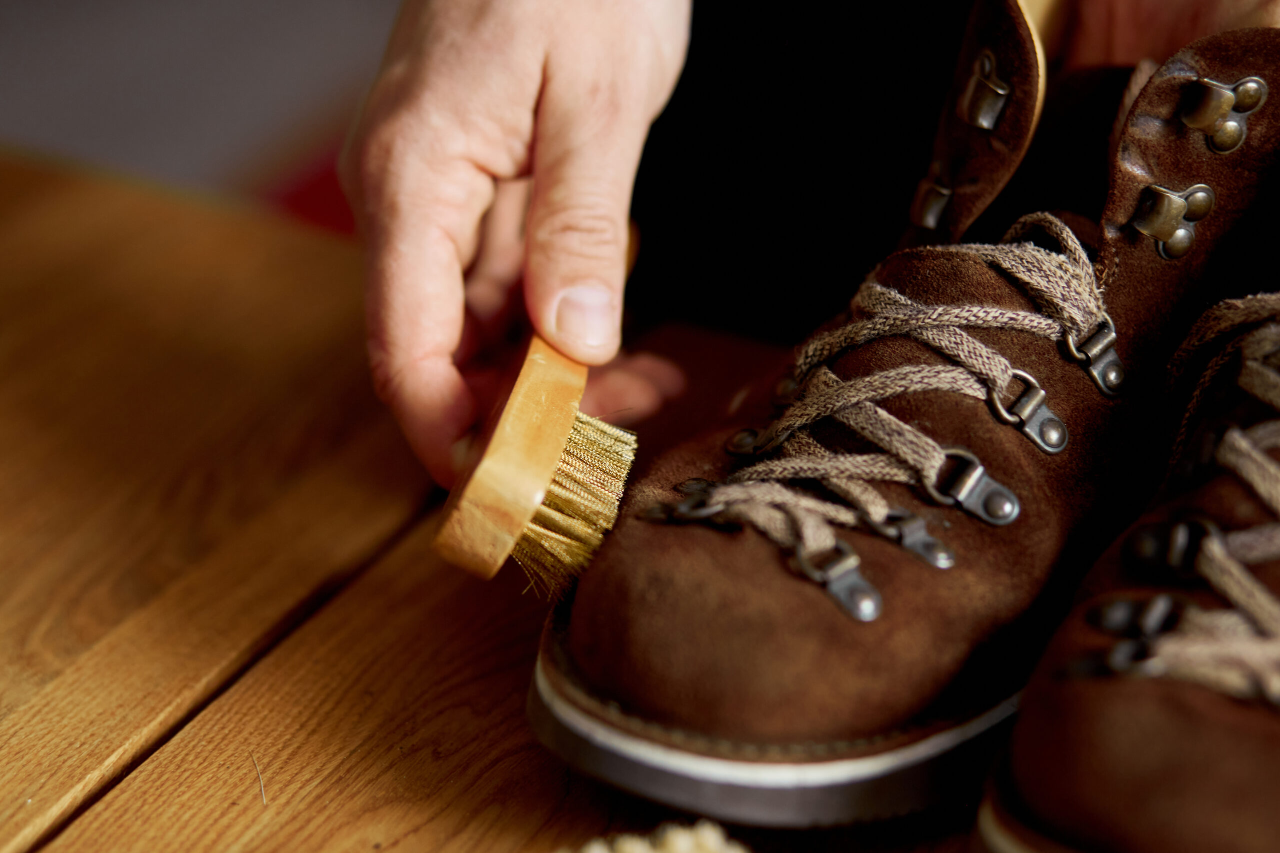 Man's hand clean suede shoes, boots with a brush on wooden background. Footwear maintenance captured, copy space, for text.