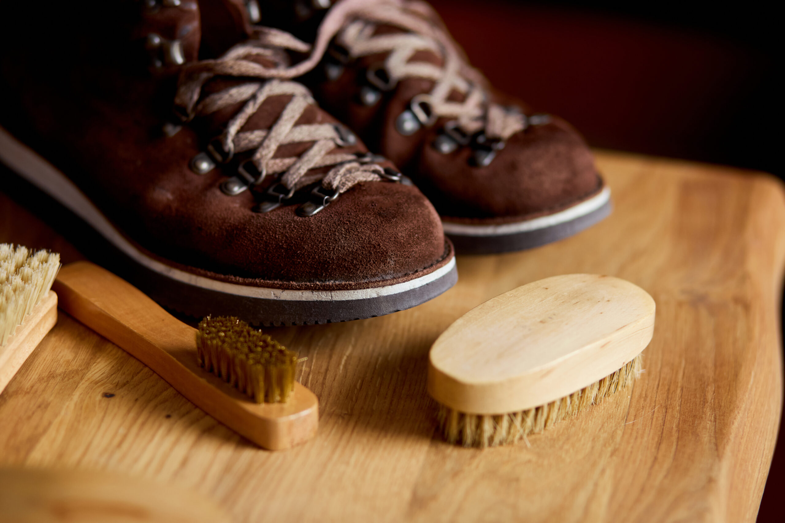 Flat lay, top view footwear with suede shoe boots care accessories, brush on wooden table. Footwear maintenance captured, copy space, for text.